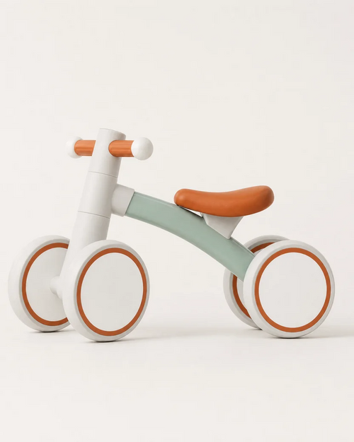Side view of the Montessori balance bike for 1 year olds, white frame with mint accents and orange padded saddle