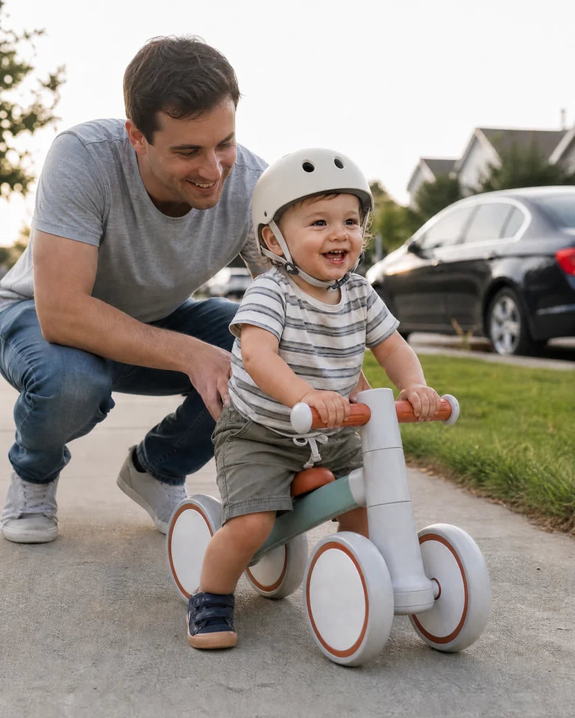 Dad guiding his helmeted baby riding the Montessori balance bike along the sidewalk