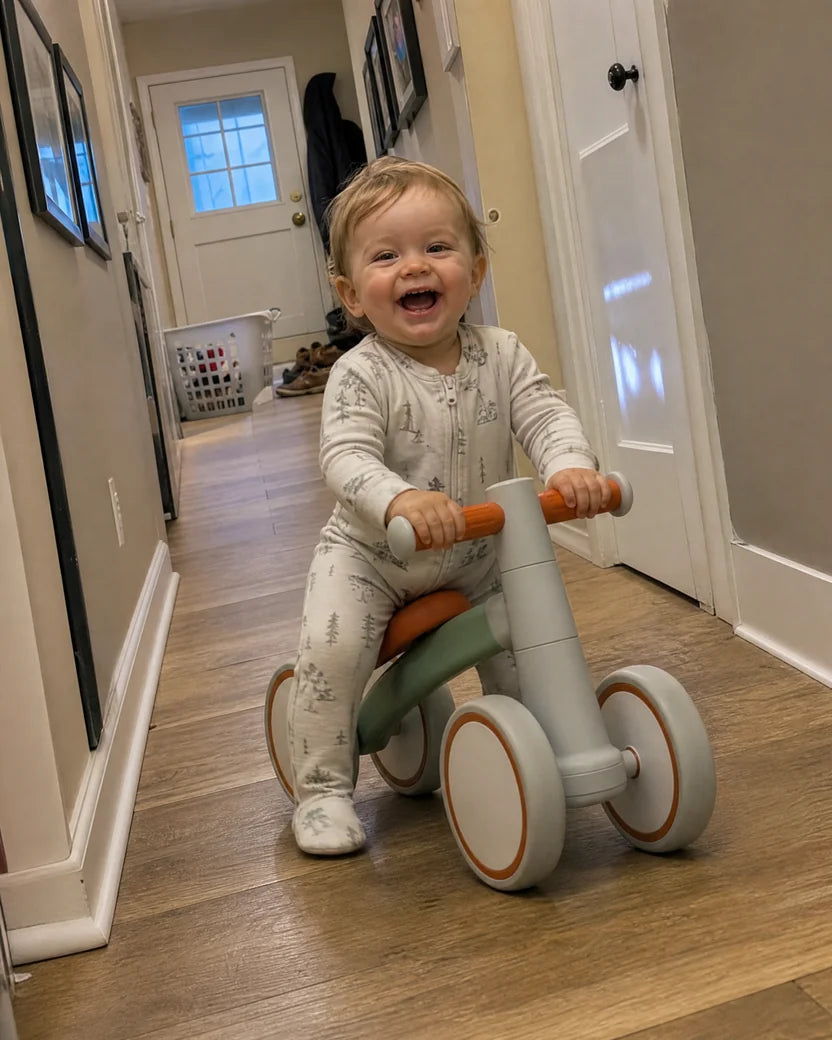 Laughing one-year-old in pajamas riding the Montessori balance bike down the hallway at home