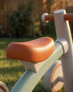Close-up of the Montessori balance bike's soft padded orange seat, outdoors in the backyard