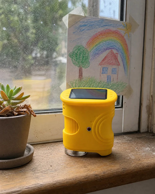 Montessori digital microscope for kids in yellow standing on a windowsill next to a potted succulent
