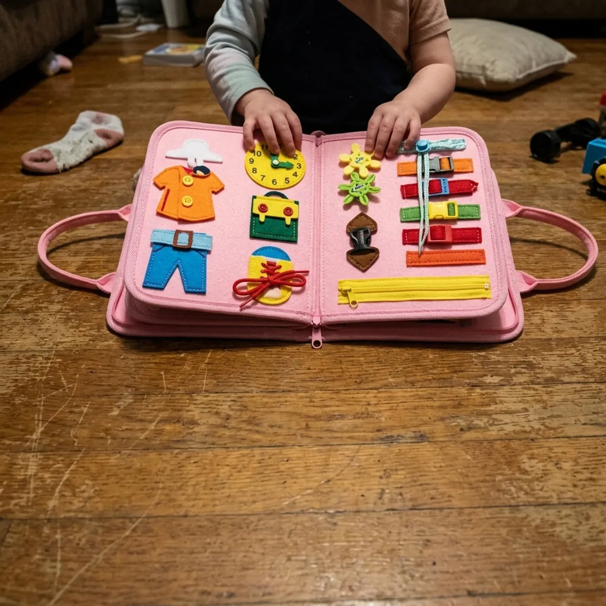 Pink felt busy book open on the floor, child's hands