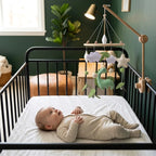 Baby lying in the crib looking up at the Green Dinosaur felt mobile